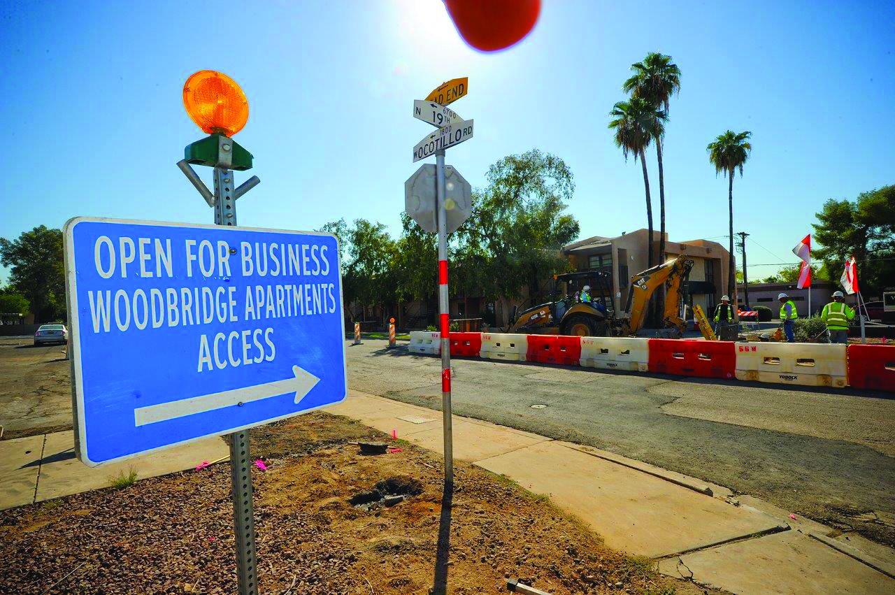 A light rail construction roadway scene is pictured with traffic barricades. In the foreground, a business access sign is visible, directing drivers to an adjacent business.