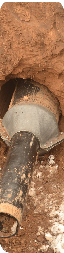 A close up image of the horizontal directional drilling drill head used to bore the tunnel for the Force Main pipe installation emerging out of a hole in the ground, surrounded by wet clay and dirt.